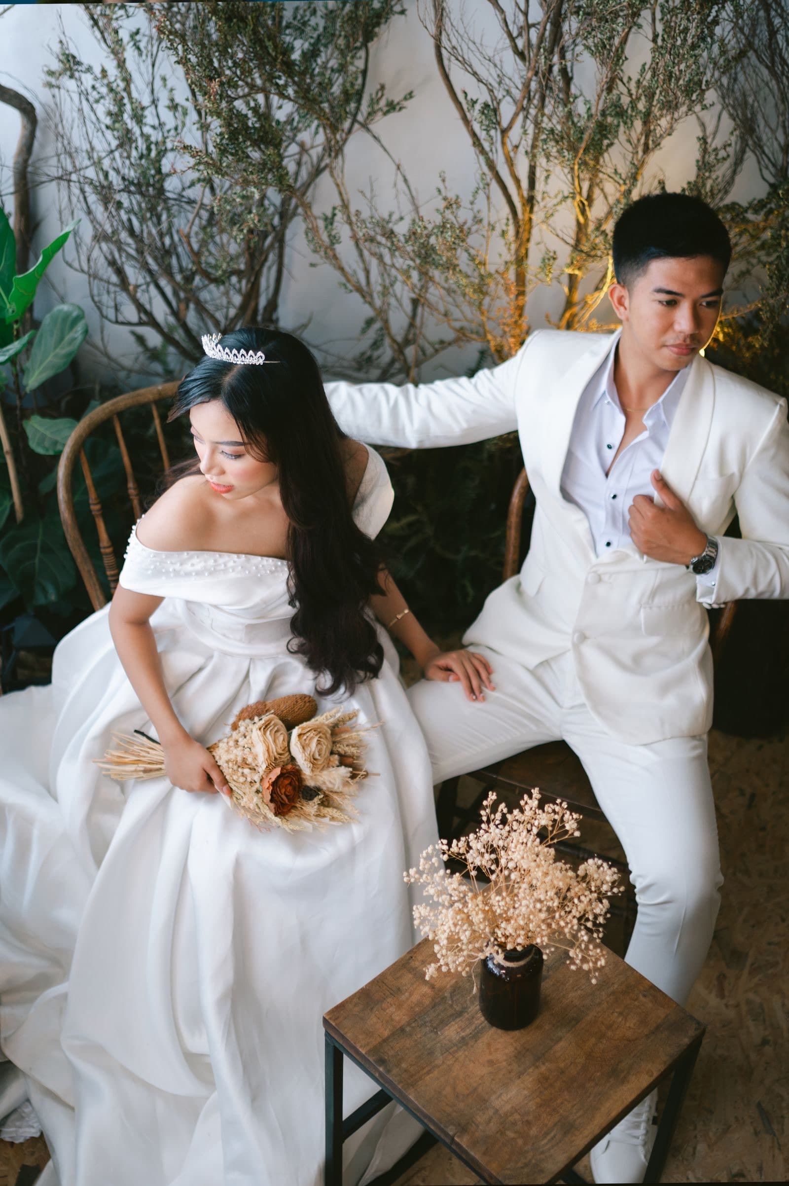 A bride and groom in white seated together with dried flowers